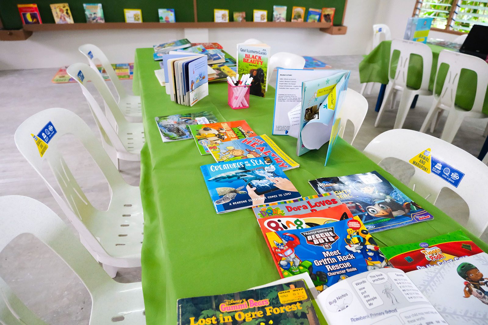 Storybooks and comics donated to the library, with a full bookshelf in the background